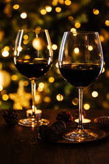 Two glasses of red wine in front of Christmas tree and lights in blurry background, festive atmosphere