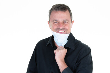 Caucasian handsome male in black shirt smiling pulling down blue surgical face mask to smile in White background