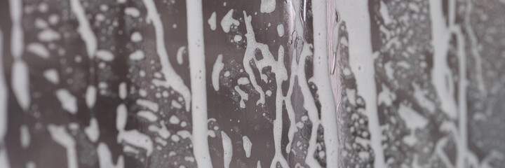 Closeup of soapy foam on transparent glass in bathroom background