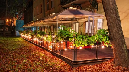 Podświetlony ogródek kawiarniany na krakowskich plantach wśród jesiennych liści - obrazy, fototapety, plakaty