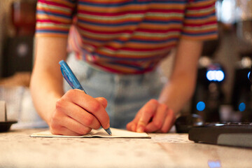 Close up of an unrecognizable bar waitress standing behind the bar counter and writing an order to the notepad.