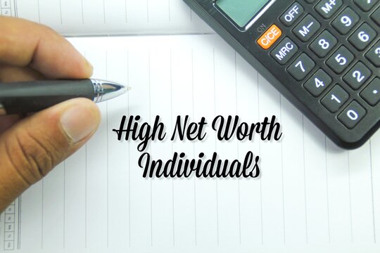 Calculator, Hand Holding Pen With The Words High Net Worth Individuals