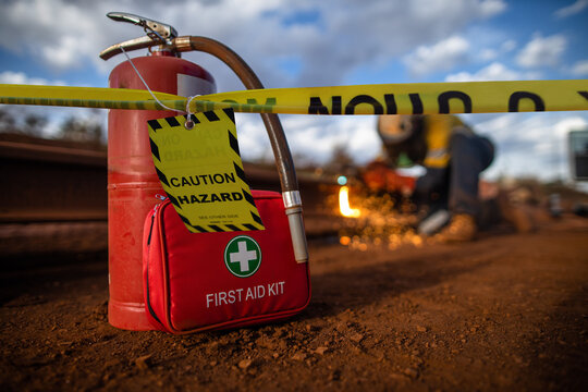 Safety Workplace Yellow Striped Caution Tape Warning Sign Barricade Exclusion Zone Preventing From Public Access First Aid Kit With Fire Extinguisher Defocused Construction Worker Using Oxy Hot Work  