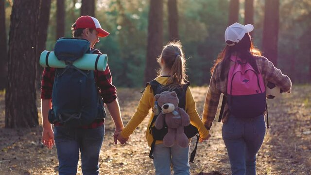 Happy family hiking through a forest. Parents with daughter walking by hiking trail. People having fun on a trekking day. Group team on hike in forest. Travel vacations and family hiking concept.