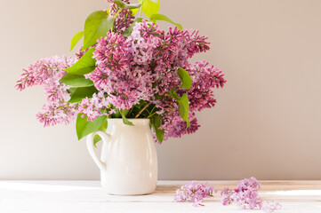 bouquet of purple lilacs in a white jug on a wooden table. spring flowers.