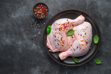 Two chicken thighs sprinkled with pepper and basil on a dark background. © Helga1