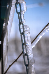 Close up of a steel chain in the vineyard covered in frozen rain in bright sunshine. Winter landscape after a freezing rain