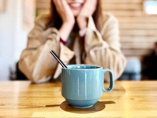 コーヒーカップの向こうで両手を頬に笑顔の女性