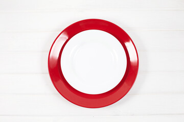 Empty ceramic red and white plates on white wood background.