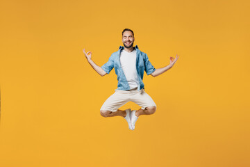 Fototapeta na wymiar Full body young smiling fun happy man 20s wearing blue shirt jump high hold spreading hands in yoga om aum gesture relax meditate try to calm down isolated on plain yellow background studio portrait