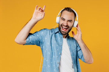Young smiling happy satisfied cool caucasian man 20s wearing blue shirt white t-shirt headphones listen to music dancing isolated on plain yellow background studio portrait. People lifestyle concept.