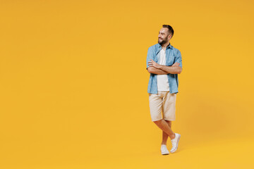 Fototapeta na wymiar Full body young smiling happy fun minded cool man 20s wearing blue shirt white t-shirt hold hands crossed folded looking aside on copy space area isolated on plain yellow background studio portrait