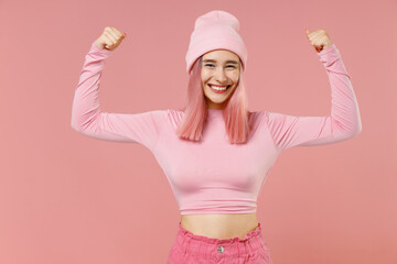 Obraz na płótnie Canvas Young woman 20s with dyed rose hair in rosy top shirt hat showing biceps muscles on hand demonstrating strength power isolated on plain light pastel pink background. People lifestyle fashion concept.