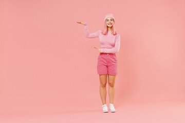 Fototapeta na wymiar Full body young woman 20s with bright dyed rose hair in rosy top shirt hat hold index finger on copy space area mock up isolated on plain light pastel pink background People lifestyle fashion concept
