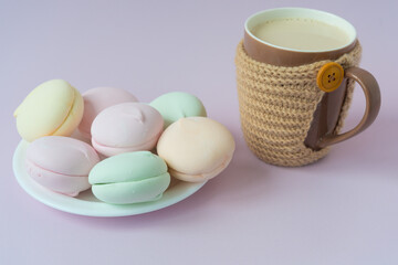 Cozy picture in pastel shades. A multi-colored marshmallow lies on a saucer. There is a cozy mug with a hot drink nearby. Mug with knitted case
