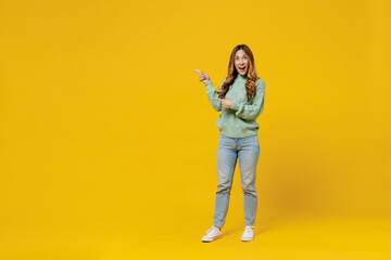 Fototapeta na wymiar Full body young surprised happy fun woman 30s wear green knitted sweater point index finger aside on workspace area isolated on plain yellow color background studio portrait. People lifestyle concept.