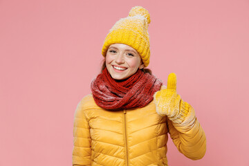 Fascinating smiling excited vivid young woman 20s years old wears yellow jacket hat mittens looking camera showing thumb up like gesture isolated on plain pastel light pink background studio portrait.