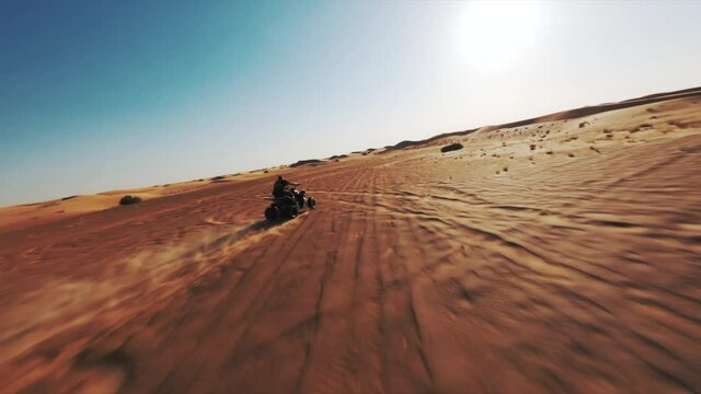 FPV drone shot tracking a All terrain vehicle driving on sunlit dunes of the Dubai Desert