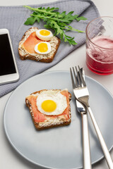 Toast with jamon and boiled quail eggs, fork and knife on gray plate.