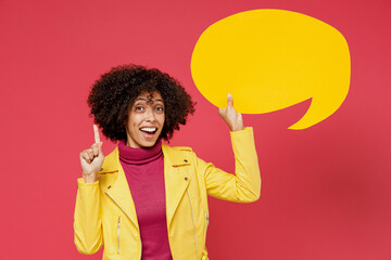 Young curly black woman 20s wears yellow jacket hold in hand empty blank Say cloud speech bubble for promotional content finger up with great new idea isolated on plain red background studio portrait.