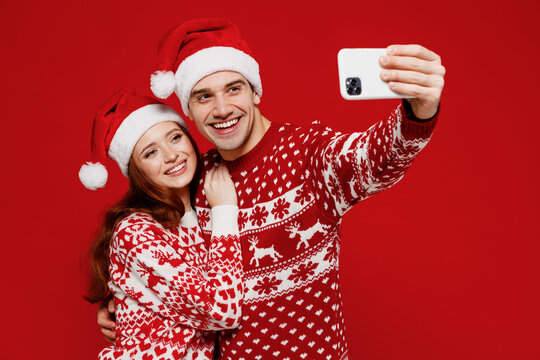 Young couple friends two man woman 20s in sweater hat doing selfie shot on mobile cell phone isolated on plain red background studio. Happy New Year 2022 celebration merry ho x-mas holiday concept