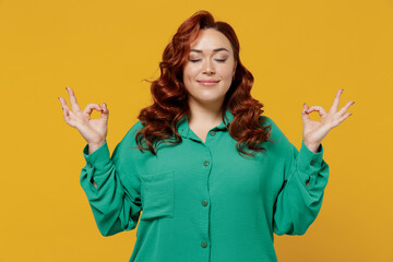 Spiritual tranquil young ginger chubby overweight woman 20s years old wears green shirt hold spreading hands in yoga om aum gesture relax meditate isolated on plain yellow background studio portrait.