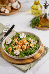 Arugula salad with shrimp and champignons, olive oil and dill on a wooden board on a white surface