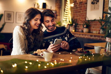Couple looking at phone together while in cafe during christmas time
