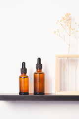 Amber glass dropper bottles with black lid on the shelf. Skincare concept on white wall background. Spa natural cosmetic concept for face body care