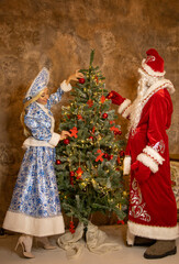 Russian Ded Moroz and Snegurochka in beautiful traditional costumes decorate a Christmas tree indoors. Christmas, new year, holidays, children's animation, actors