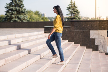 A young, beautiful and attractive Caucasian brunette girl in a yellow sweater climbing up the...