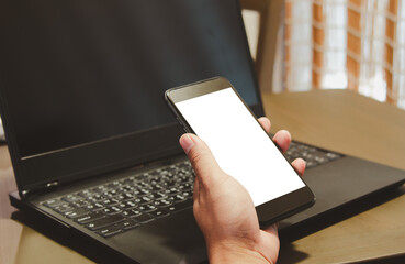 mock up hand holding smartphone white blank screen and computer laptop on the desk.