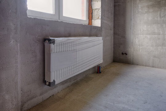 Metal heating radiator in a country house under construction. White radiator under the window against the background of walls sheathed with heat-insulating material