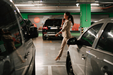 Businesswoman in suit unlocking car on parking. Beautiful woman talking to the phone..