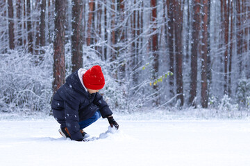 Fototapeta na wymiar A child in a red hat plays in the snow in the winter forest