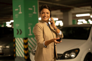 Businesswoman in suit unlocking car on parking. Beautiful woman talking to the phone..