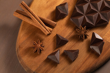 Dark bitter chocolate is broken into pieces. Decorated with cinnamon sticks. Brown background....
