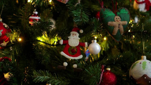 Santa Claus decoration on a Christmas tree with other red, green and white decorations surrounding it. Rack focus image with beautiful soft focus. Festive footage of Christmas decorations.