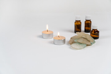 Fototapeta na wymiar sea salt, two candles and aromatic oils in bottles on a white background. Accessories for massage in the spa salon. The concept of cosmetic procedures.