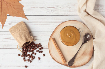 cup of dalgona coffee on wooden table with bag of natural coffee beans and cinnamon stick