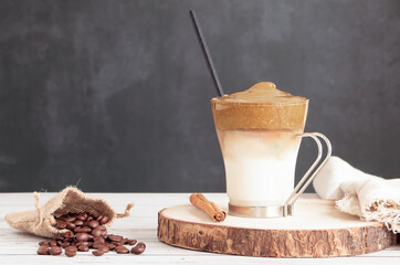 cup of dalgona coffee on wooden table with bag of natural coffee beans and cinnamon stick