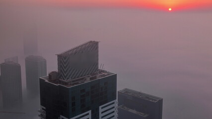 Rare early morning winter fog above the Dubai Marina skyline and skyscrapers lighted by sun aerial timelapse.