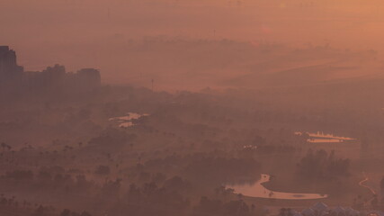 Aerial view to Golf course with green lawn and lakes, villas covered by morning fog timelapse.