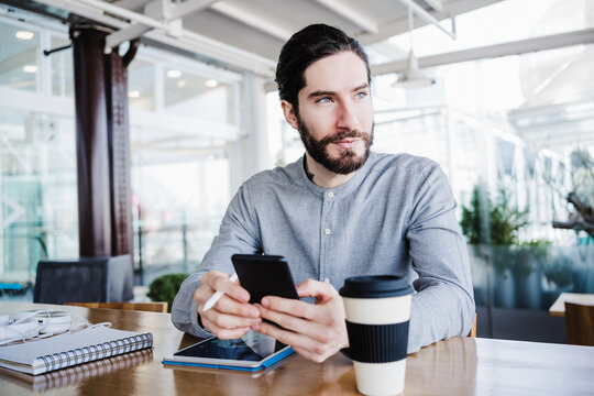 Contemplative male entrepreneur looking away while sitting with wireless technologies at work place