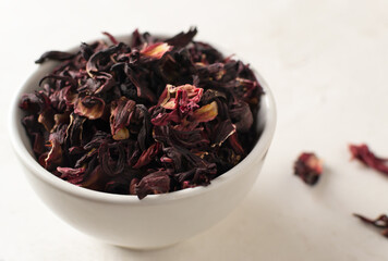 Dry leaves of hibiscus lie in a white bowl on a white background. Dried rosella or Sudanese rose flowers. It is very popular in Arab countries. Alternative medicine concept. Copy space.