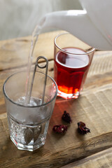 The process of brewing red hibiscus tea. Two glass glasses are on a wooden table. Rosella or Sudanese rose flowers are a very popular drink in Arab countries. Traditional drinks concept.