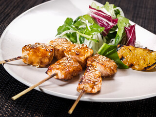 portion of salmon skewers fried in sauce yakitori with salad mix and slice of grilled lemon on a plate
