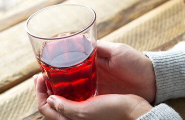 Female hands hold a glass of cold red hibiscus tea. Traditional drinks concept. The drink has a bright red color thanks to the flowers of the Sudanese rose. Horizontal orientation.