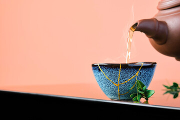 Hot green tea is poured from a ceramic teapot into a bowl. Selective focus on the blue cup. Steam...