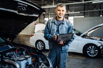 Car service, repair, maintenance concept. Portrait of positive friendly car mechanic using a...